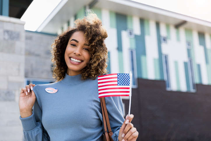 Woman smiles for camera and shows off "I voted" sticker